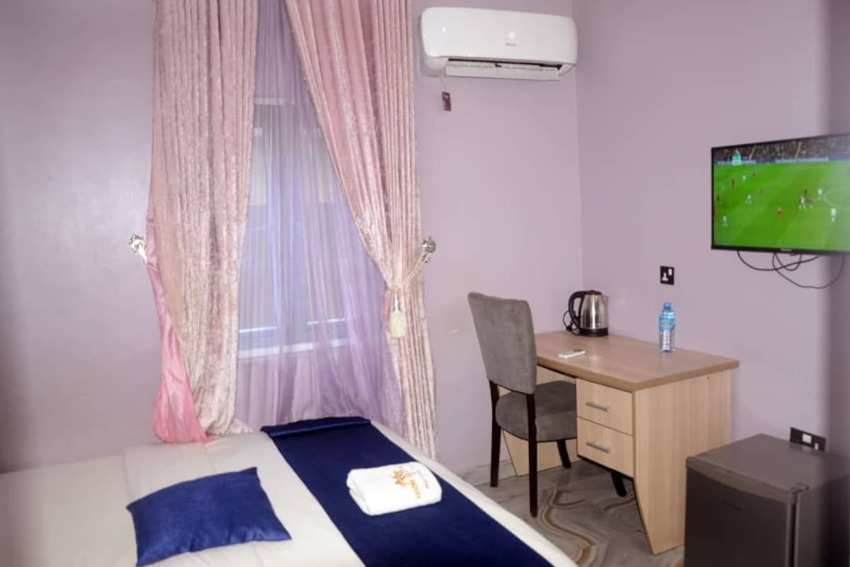 Quarto de hotel com cama, escrivaninha, cadeira, ar-condicionado, televisão e um pequeno armário.