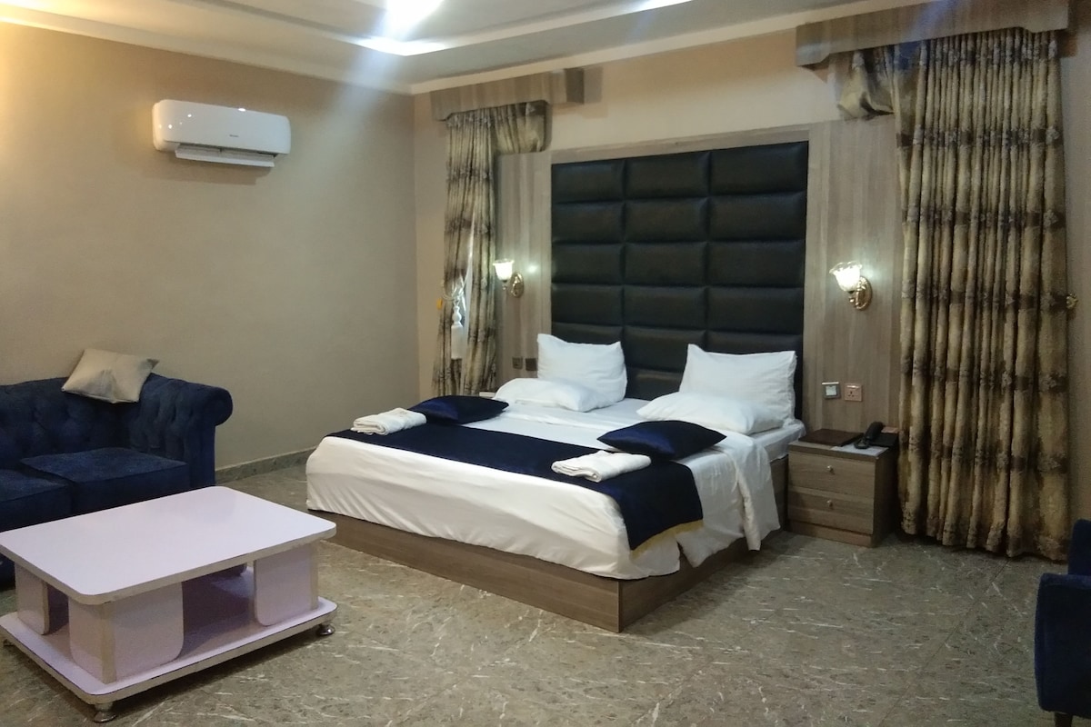 Quarto de hotel com cama, mesa de cabeceira e um pequeno espaço de estar com uma mesa.
