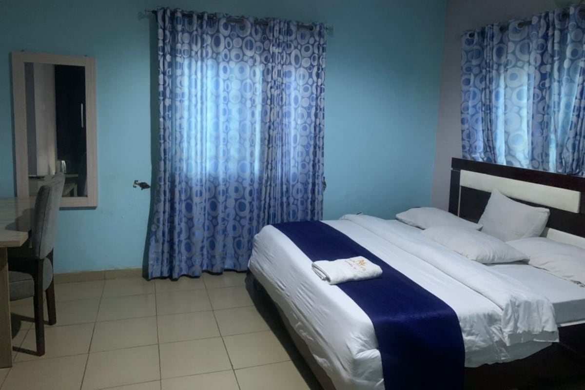 Quarto de hotel com cama, escrivaninha e cortinas.