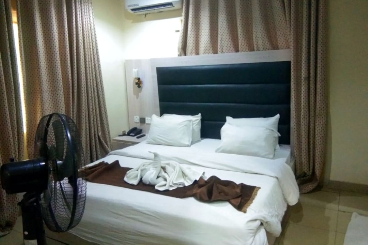 Quarto de hotel com cama, cortinas, ar condicionado e ventilador.
