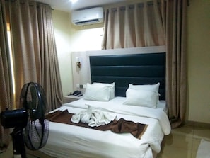 Quarto de hotel com cama, cortinas, ar condicionado e ventilador.