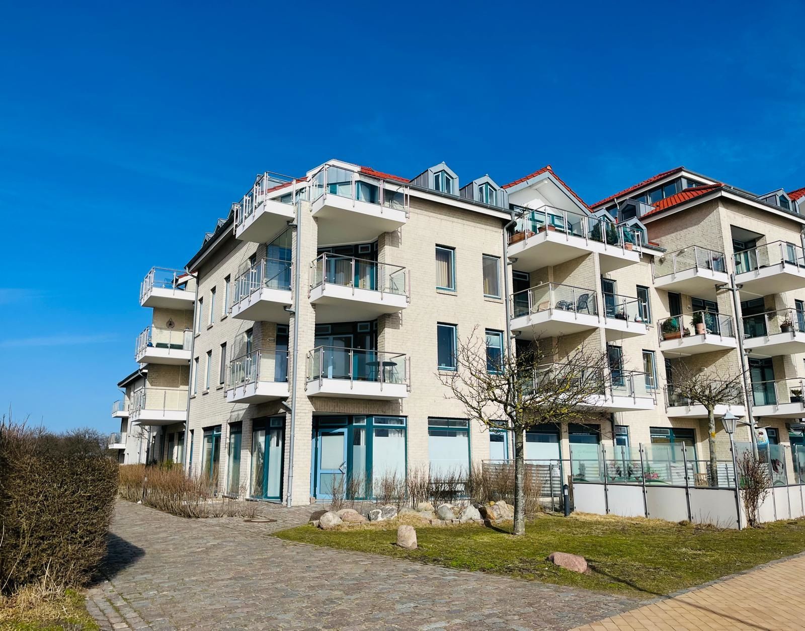 A multi-story residential building with balconies, a paved walkway, and a clear sky.
