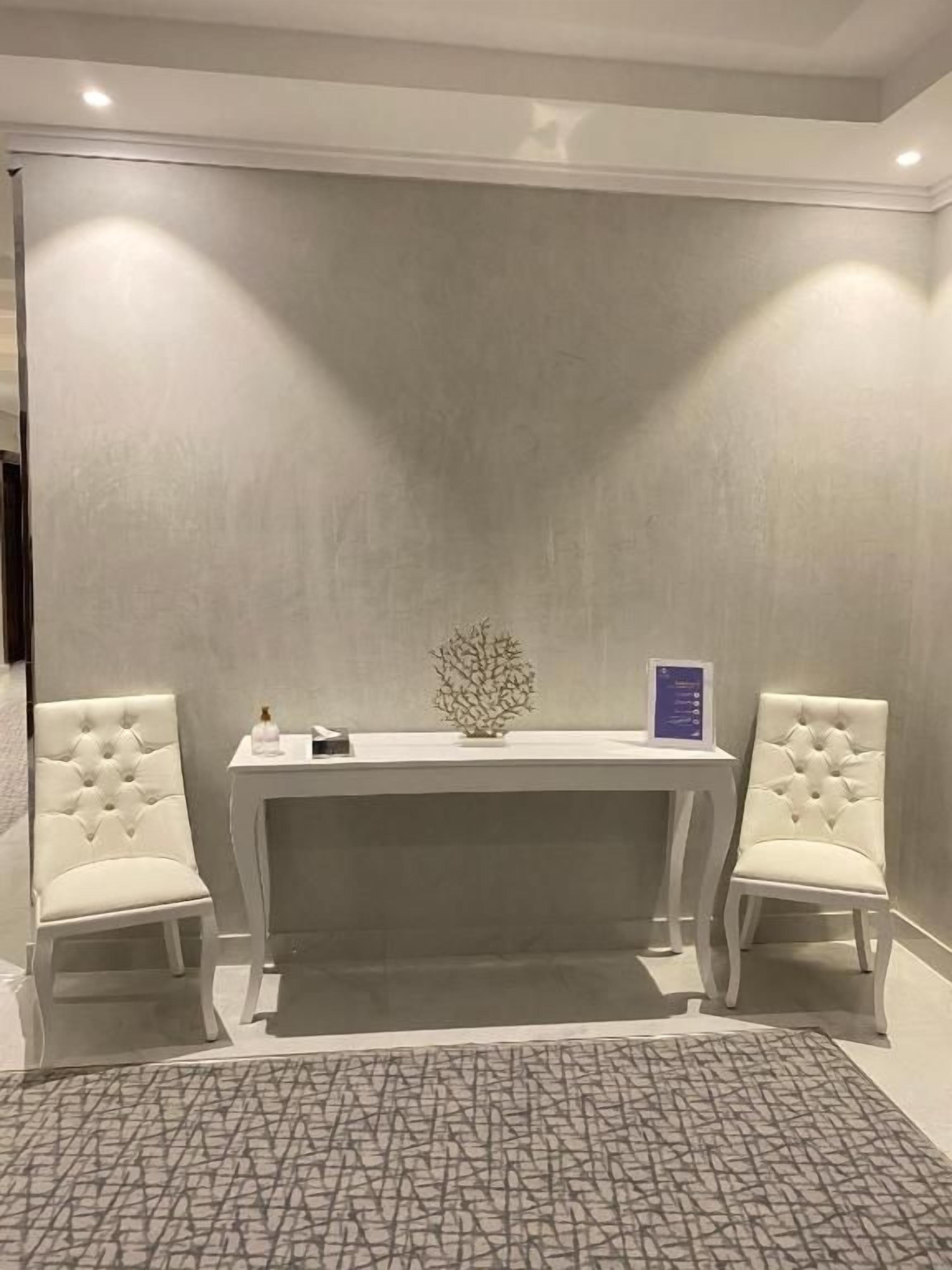 Una habitación con una silla tapizada de blanco, una mesita con un objeto decorativo y una alfombra estampada en el suelo.