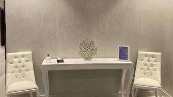 Una habitación con una silla tapizada de blanco, una mesita con un objeto decorativo y una alfombra estampada en el suelo.