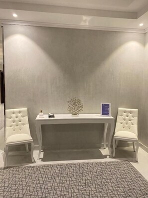 Una habitación con una silla tapizada de blanco, una mesita con un objeto decorativo y una alfombra estampada en el suelo.