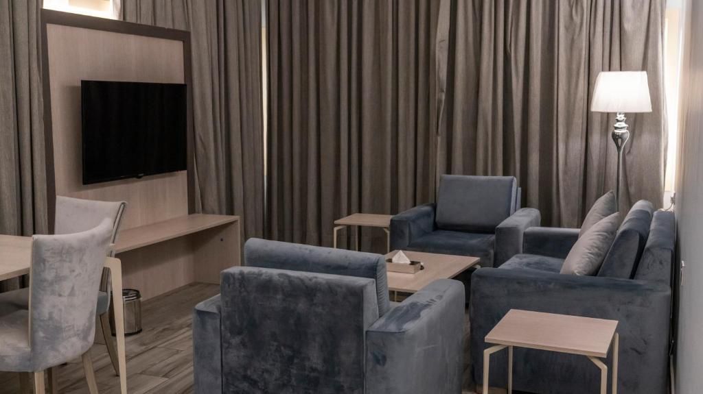 A modern hotel room with a flat-screen TV mounted on the wall, a sofa set, a small table, and a lamp.