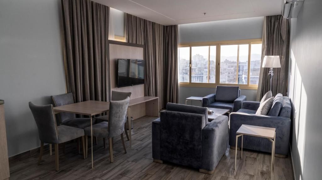 Habitación de hotel moderna con zona de comedor, sofá, televisión de pantalla plana y vistas a la ciudad.