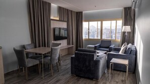 Habitación de hotel moderna con zona de comedor, sofá, televisión de pantalla plana y vistas a la ciudad.