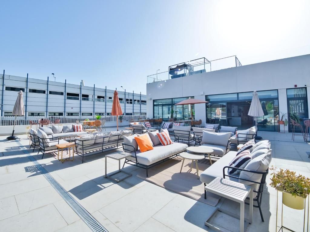 A rooftop terrace with outdoor seating, a modern building in the background, and a clear sky.