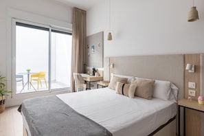 A hotel room with a bed, a desk, a chair, a potted plant, and a view through a sliding door. - Canvas Sevilla Lago (Sevilla)