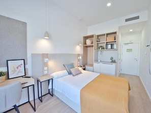 A modern hotel room with a bed, desk, and kitchenette. - Canvas Sevilla Lago (Sevilla)