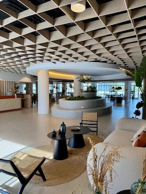 Un hall espacioso con un diseño de techo moderno, una zona de estar central y una jardinera circular con plantas.
