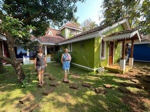 A traditional house with a tiled roof, a porch, and a small garden area with stepping stones. - The Amrit Goa (Candolim)