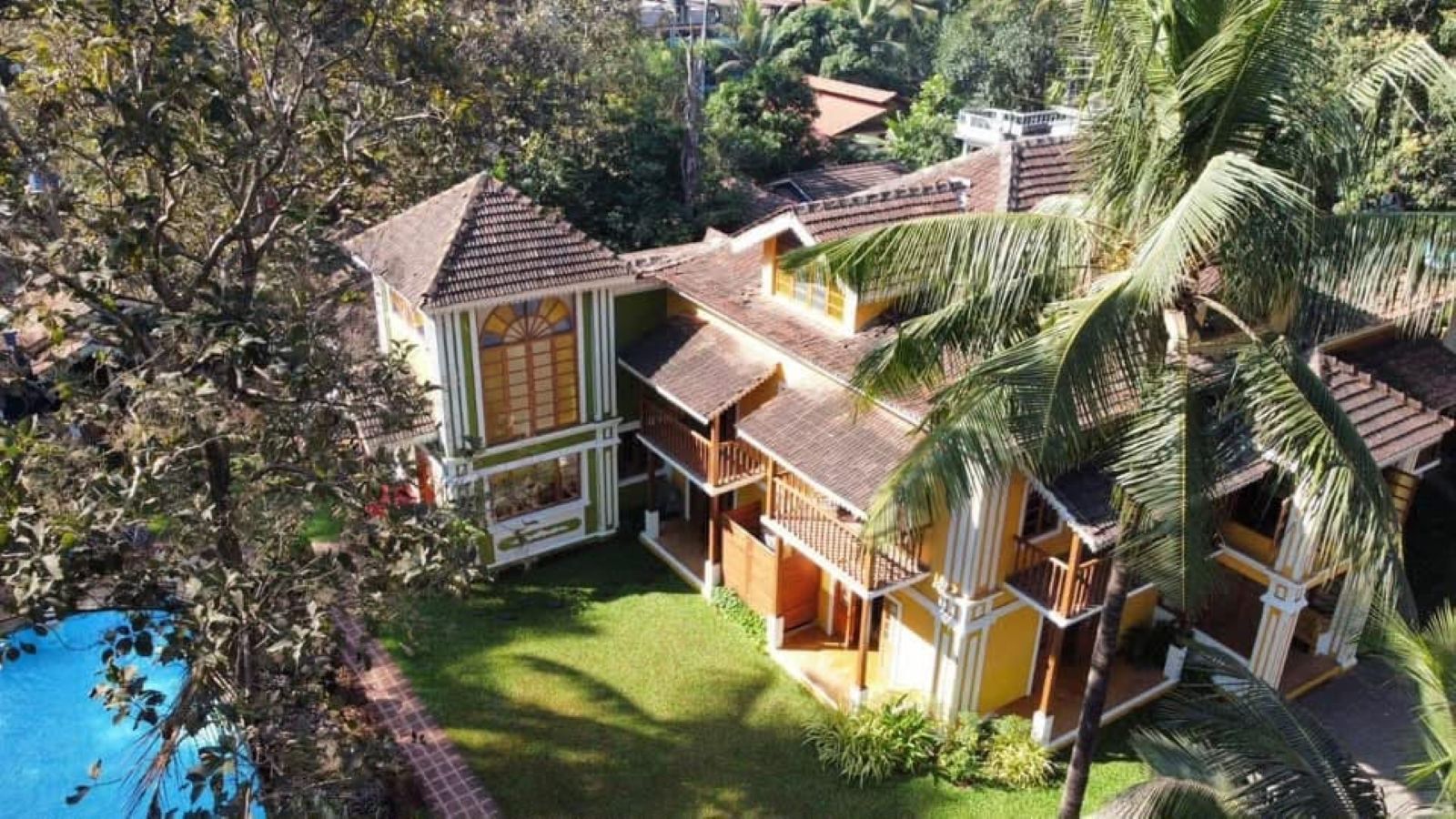 Un edificio de varios pisos con piscina, rodeado de exuberante vegetación y palmeras.