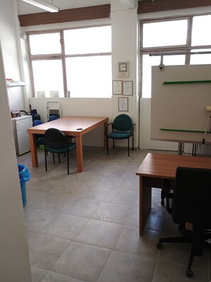 Een kamer met een houten tafel, twee stoelen, een whiteboard en een raam met jaloezieën.