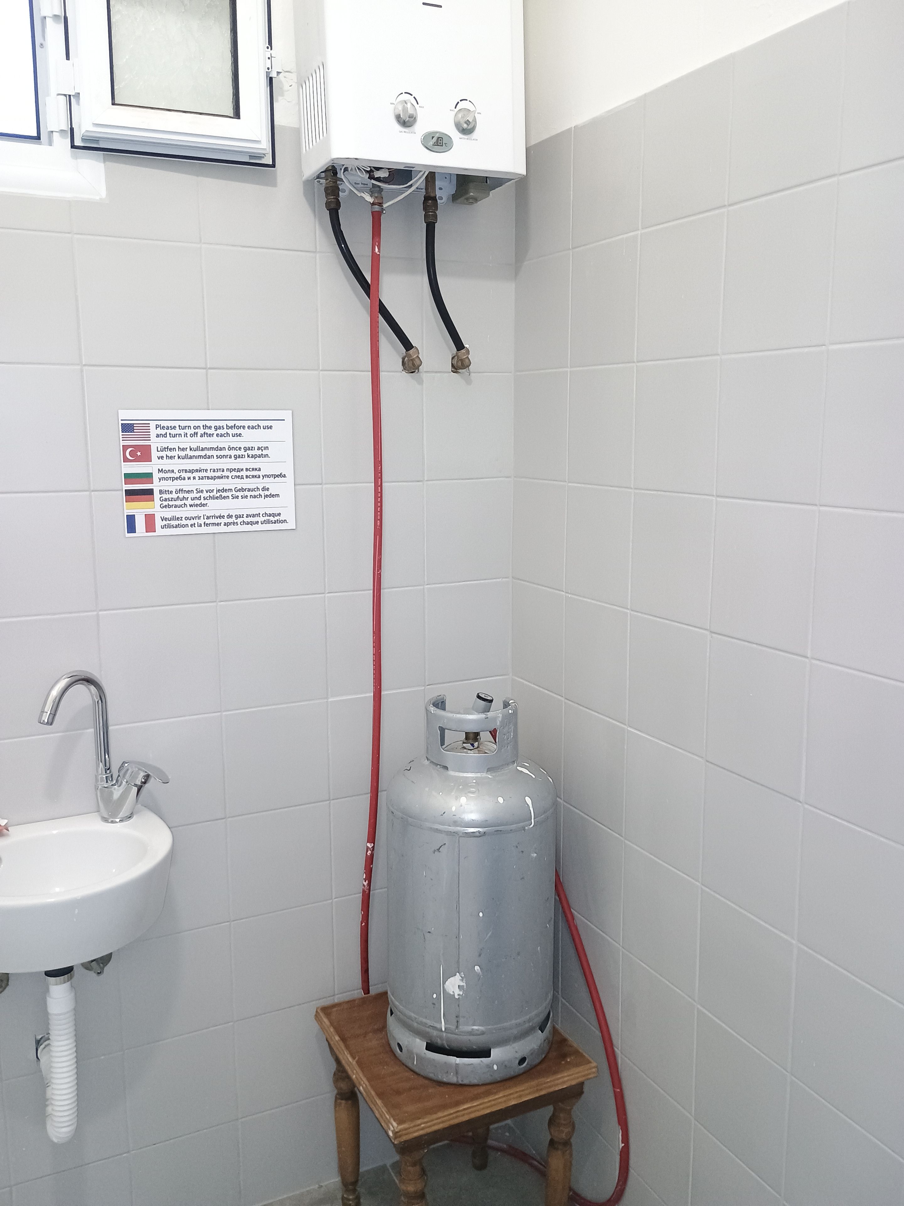 Een badkamer met een gasverwarmer, een wastafel en een bord met meertalige instructies.