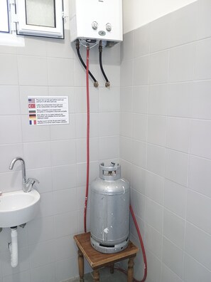 A bathroom with a gas heater, a sink, and a sign with multilingual instructions. - thomasbnb alexandroupolis (Alexandroupoli)