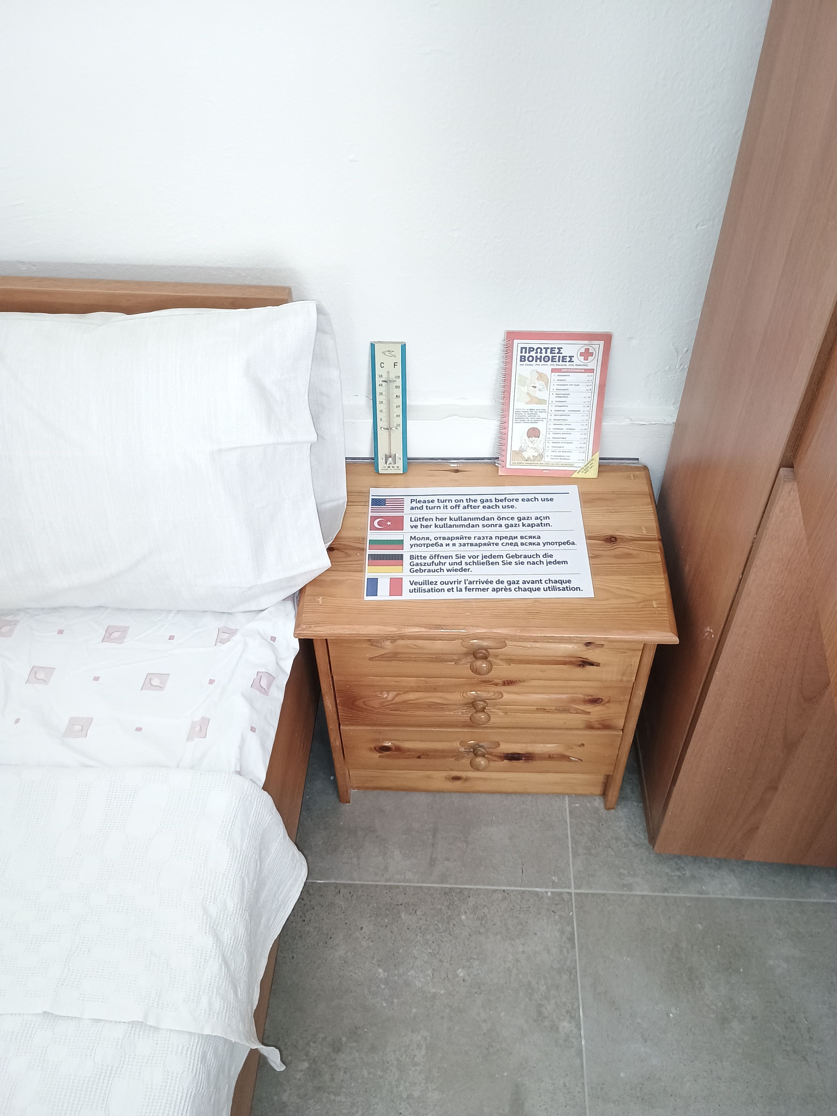 Een houten nachtkastje met een thermometer, een verbanddoos en een meertalige instructiekaart.