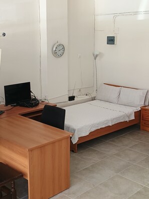 Een kamer met een bed, een bureau, een stoel, een klok en een lamp.