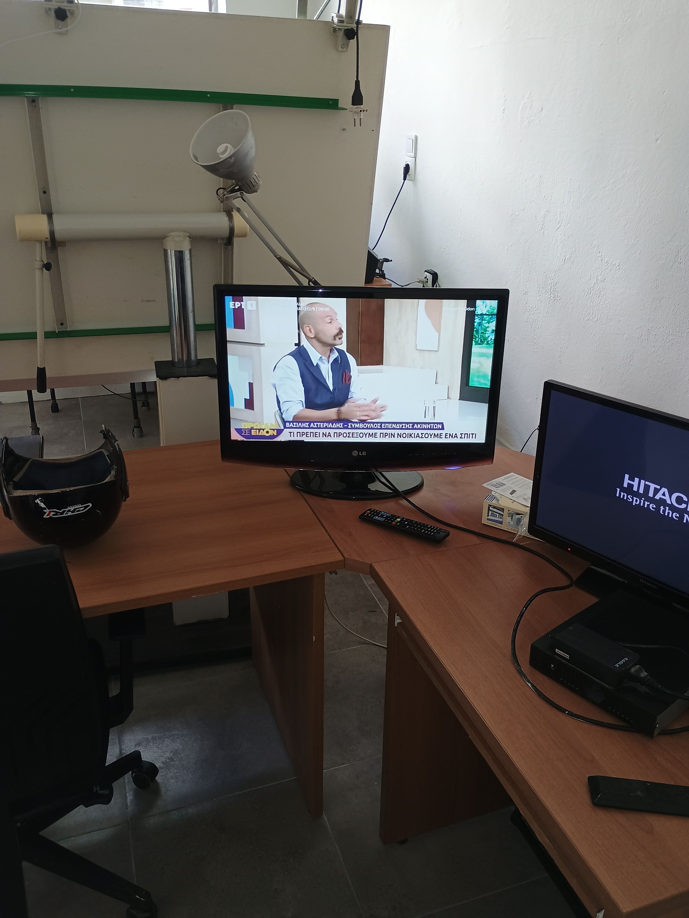 Une pièce avec un téléviseur diffusant un programme d’information, un bureau avec un casque, une télécommande et un écran d’ordinateur.