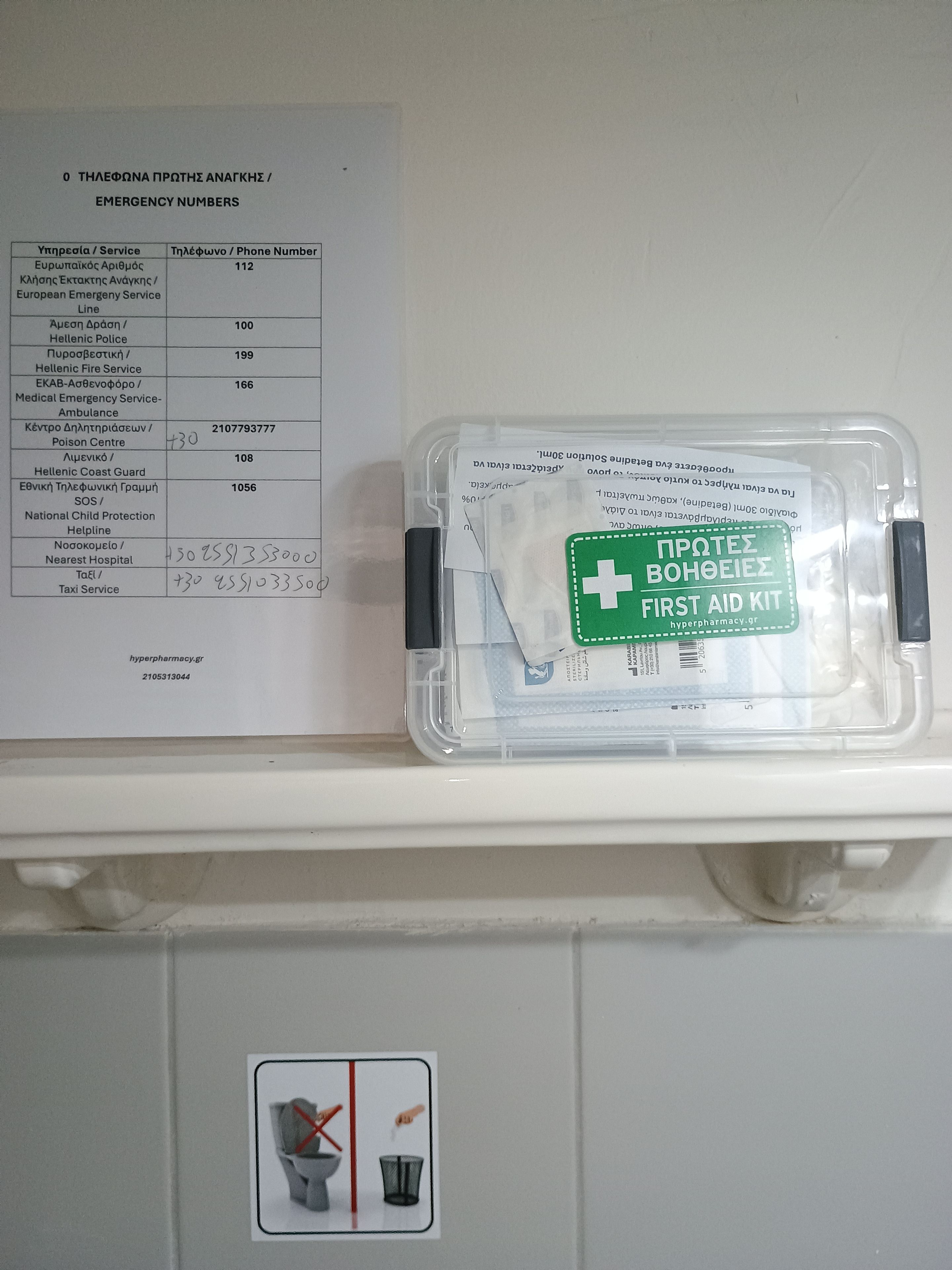 Une étagère blanche sur laquelle figure une liste de numéros d’urgence et une trousse de premiers secours.
