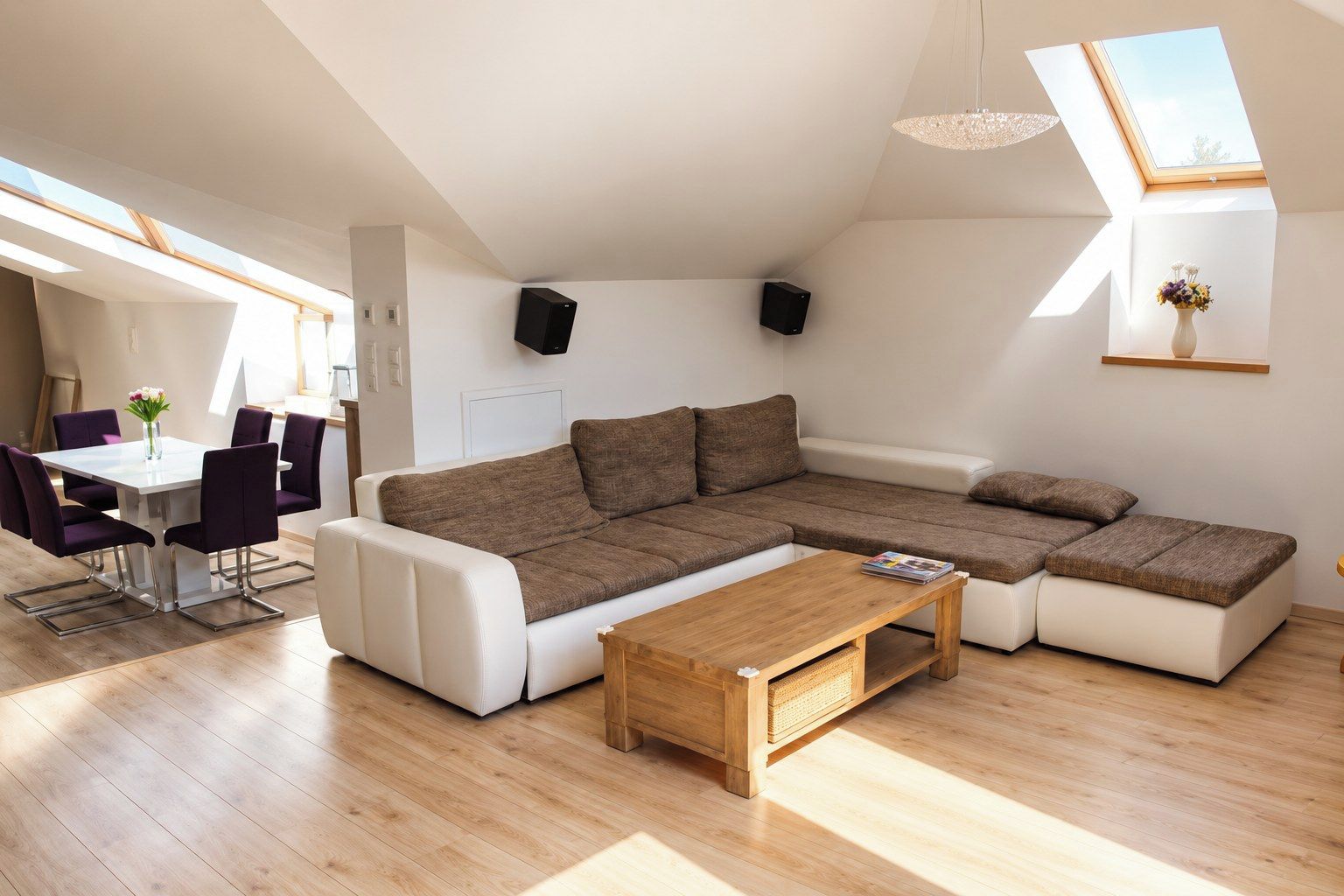 Um espaço de estar moderno com sofá modular, mesa de jantar com cadeiras e um claraboia.
