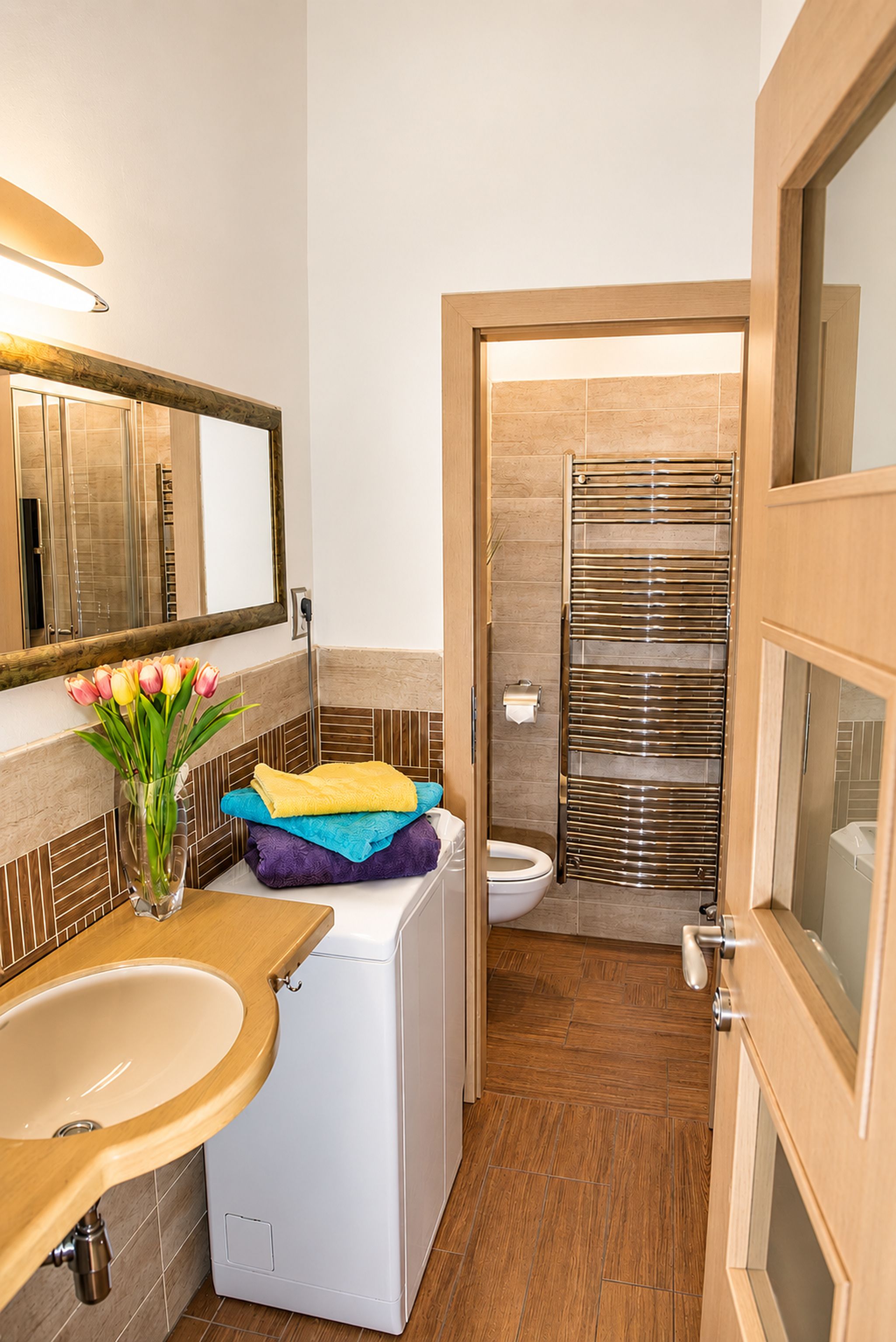Ein kleines Badezimmer mit einem Holzwaschtisch, einer weißen Waschmaschine, einer Toilette und einer Duschkabine.