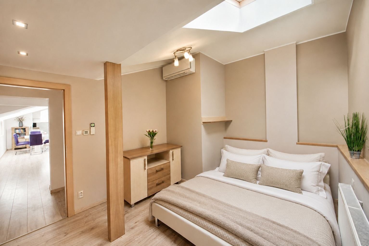 A modern bedroom with a skylight, a bedside table with a vase, a bed with multiple pillows, and a radiator.