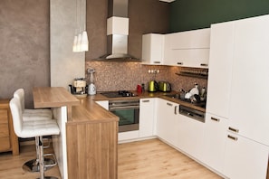 A modern kitchen with white cabinets, a wooden countertop, a built-in oven, and a coffee machine. - Cassovia City Park Residence (Košice)