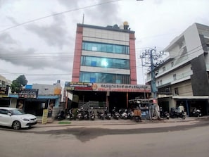 Un edificio de varios pisos con bar y restaurante en la planta baja, varias motocicletas estacionadas y un automóvil blanco en la calle.