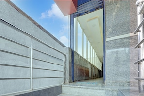 Una entrada moderna de edificio con barandilla metálica, puerta de cristal y una alfombra estampada en los escalones.