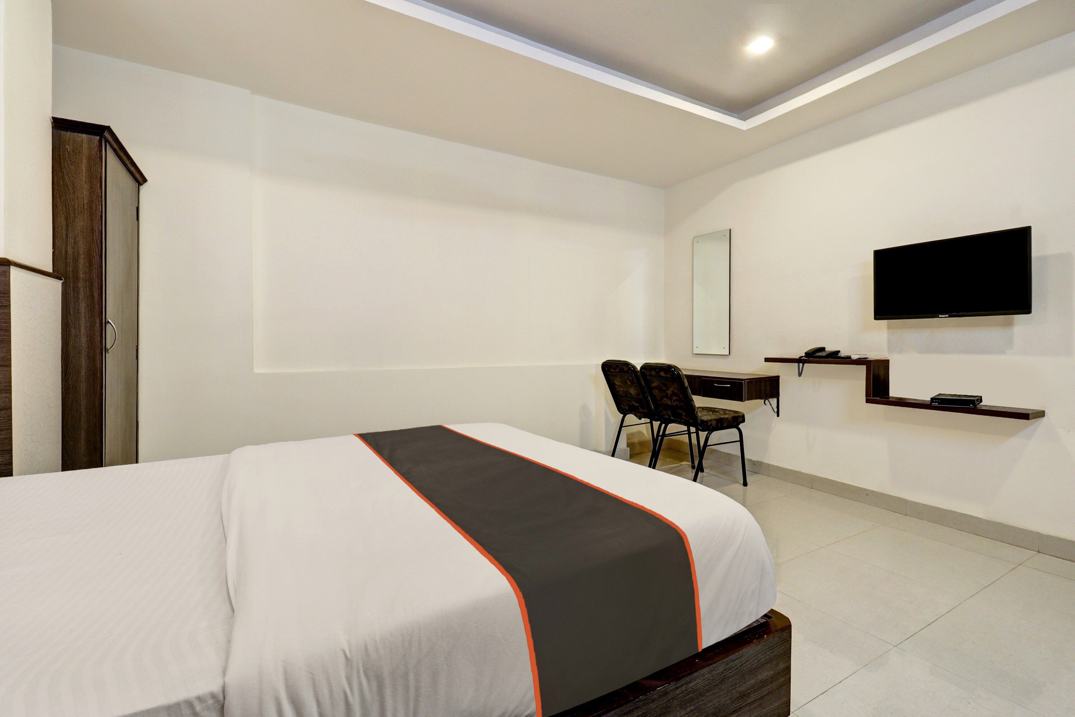 A hotel room with a bed, a desk, a chair, a television, and a wardrobe.