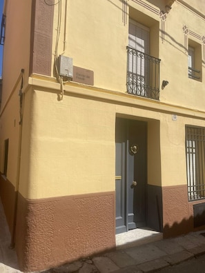 Un immeuble à la façade jaune, avec une partie inférieure de couleur marron et une porte ornée d’un heurtoir en laiton.