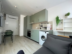 Une cuisine compacte équipée d’un lave-linge, un coin repas avec une table et des chaises, et un espace de vie avec un canapé.