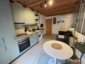 Une cuisine compacte équipée d’un lave-linge, un coin repas avec une table ronde et un canapé.