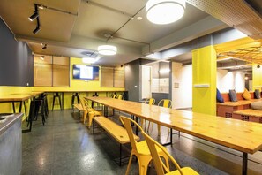 A spacious room with a long wooden table and yellow chairs, equipped with ceiling lights and a television screen. - Collection O LOCL Colive & Work Sarjapur (Bengaluru)