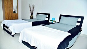 Two single beds with white and grey bedding, a wooden wardrobe, a vase with reeds, and a small blue table with a plant. - Collection O LOCL Colive & Work Sarjapur (Bengaluru)