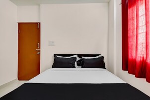 Una cama individual con ropa de cama blanca, una puerta de madera y una cortina roja.
