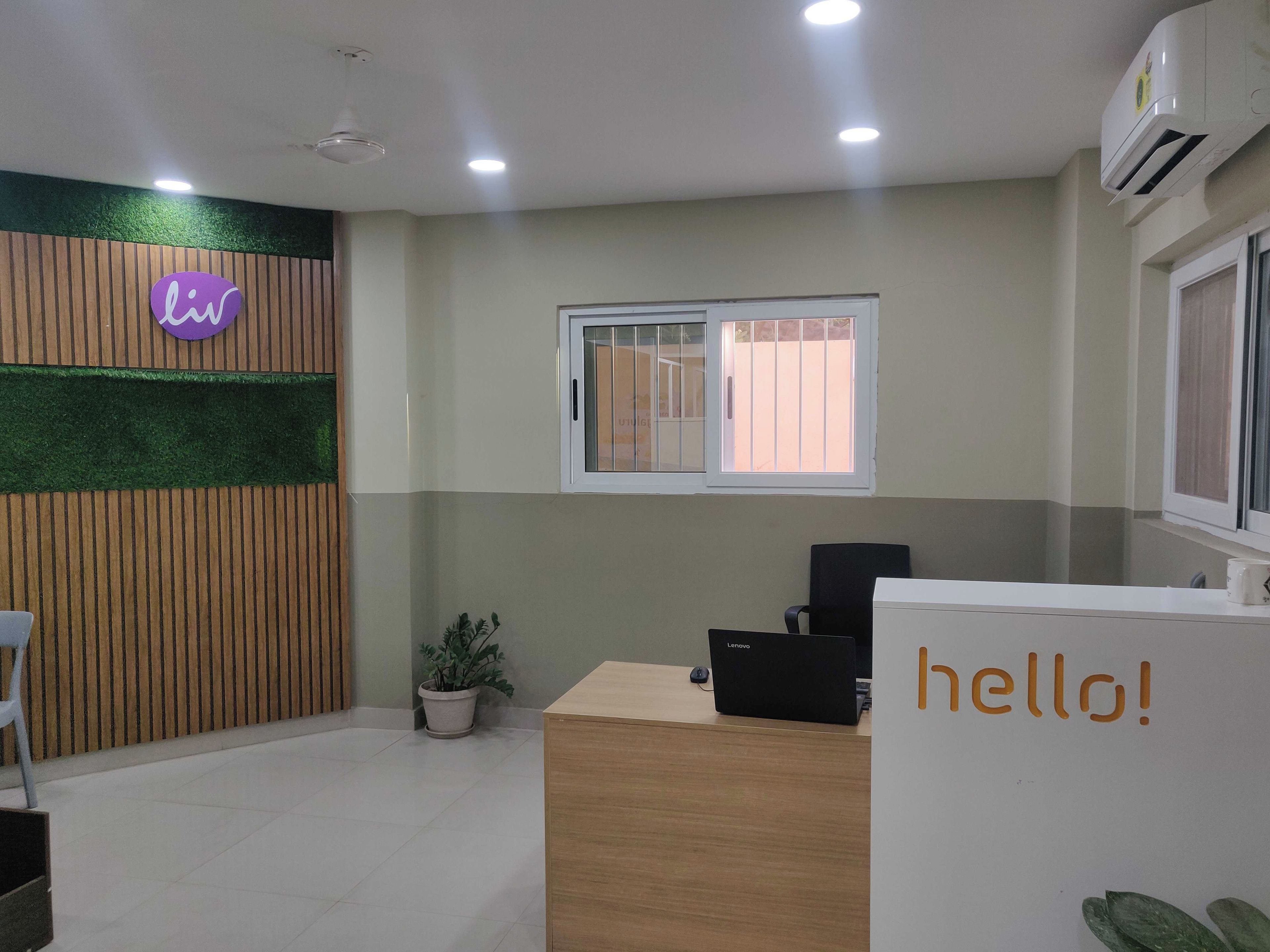 A reception area with a desk, a potted plant, a sign with 'hello!', and a window with bars.
