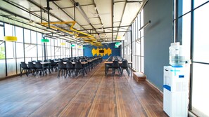 A spacious indoor area with rows of tables and chairs, large windows, and a ceiling with exposed beams and lighting fixtures. - Hotel O Local Square Manyata (Bangalore)