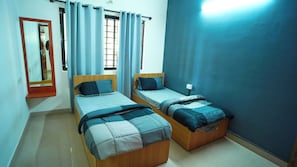 A bedroom with two wooden beds, a mirror, a window with curtains, and a wall-mounted light. - Hotel O Local Square Manyata (Bangalore)