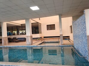 Una piscina interior amb aigua cristal·lina, envoltada d'zones d'estar i una paret de rajola.