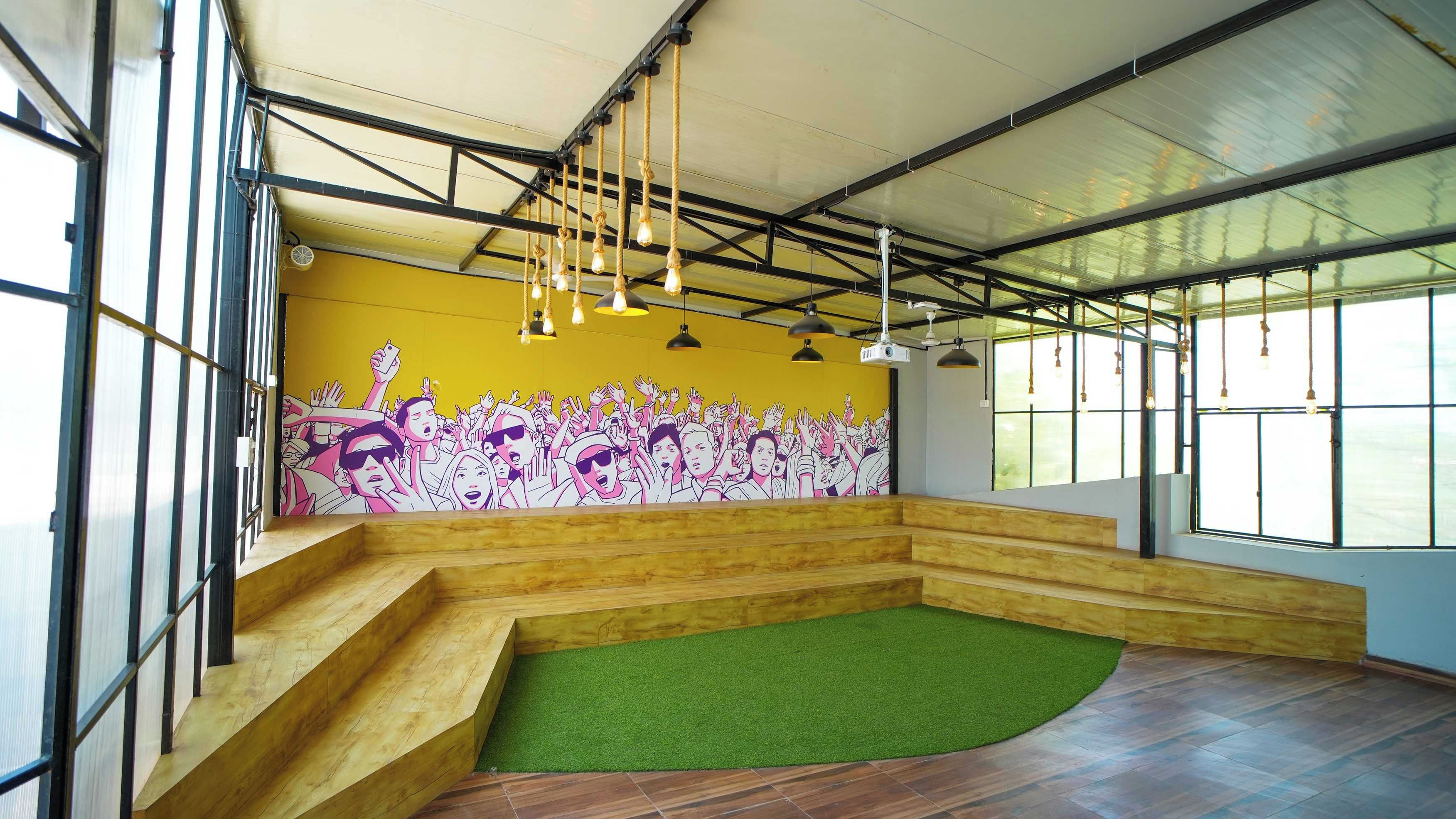 A room with a mural, wooden steps, a green carpet, and hanging lights.