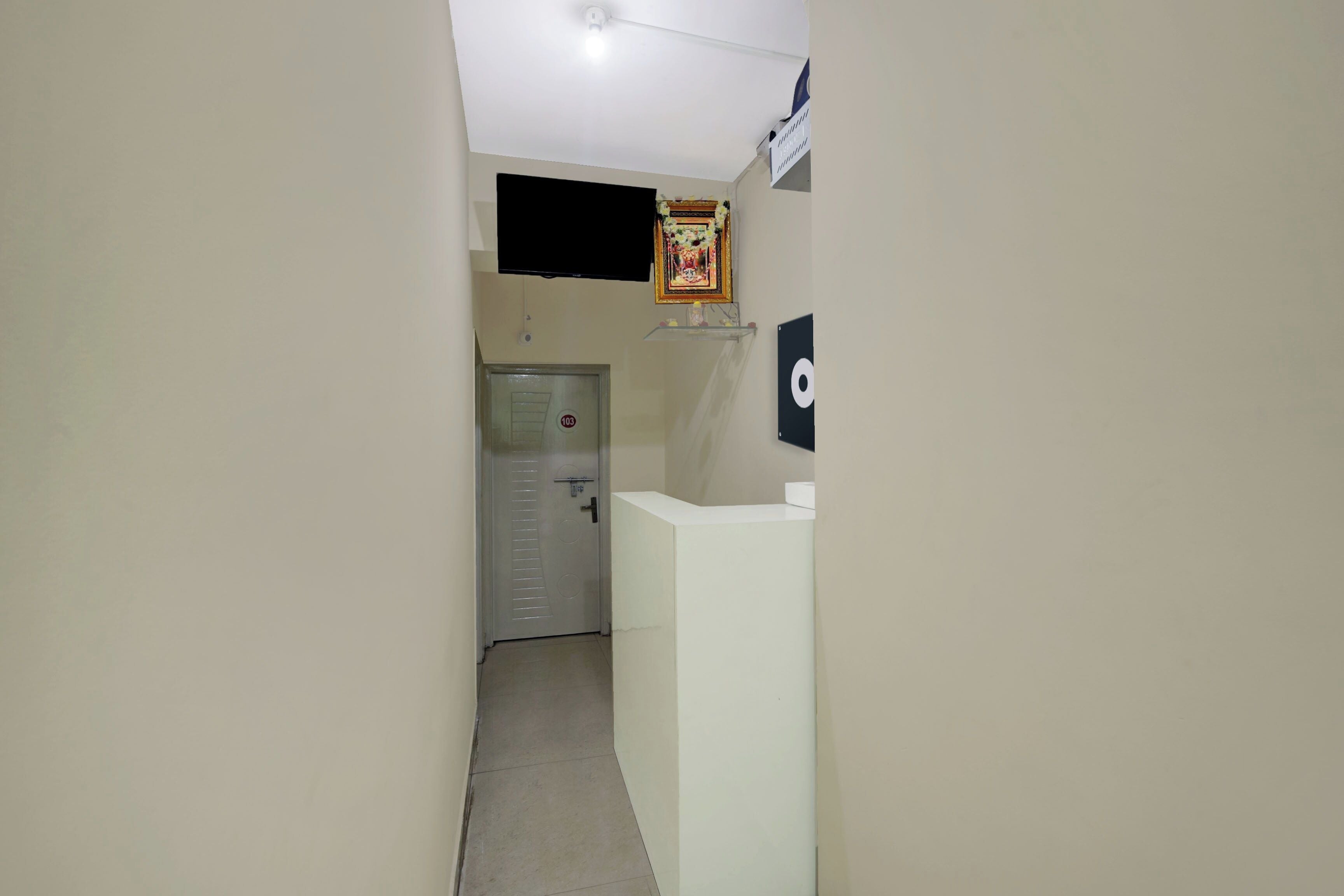 A hallway with a reception desk, a door with a number plate, and a wall-mounted television.