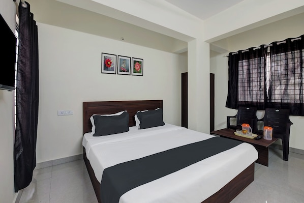 Habitación de hotel con una cama grande, una mesita de noche con bandeja, un televisor y una ventana con cortinas.