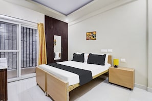 Quarto com cama, mesa de cabeceira e janela com cortinas.