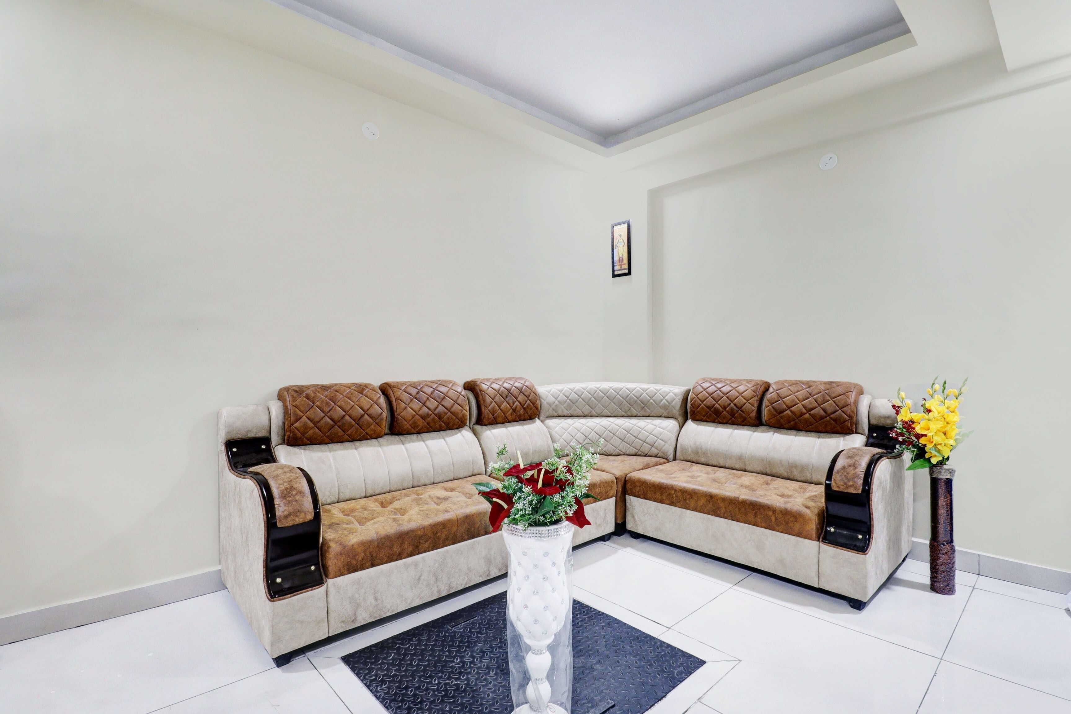 Una sala de estar en esquina con un sofá modular, un jarrón decorativo con flores y un cuadro en la pared.