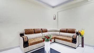 Una sala de estar en esquina con un sofá modular, un jarrón decorativo con flores y un cuadro en la pared.