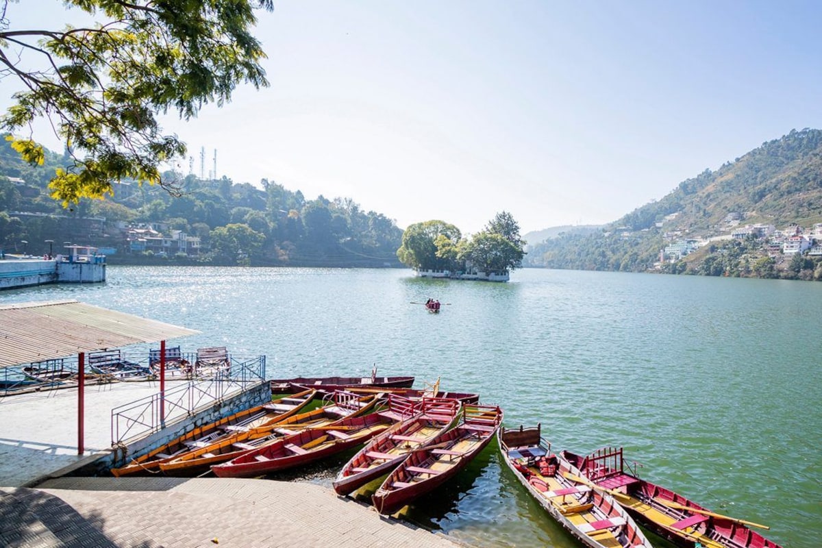 Um lago tranquilo com barcos atracados num cais, rodeado por colinas e uma pequena ilha com árvores.