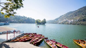 Um lago tranquilo com barcos atracados num cais, rodeado por colinas e uma pequena ilha com árvores.